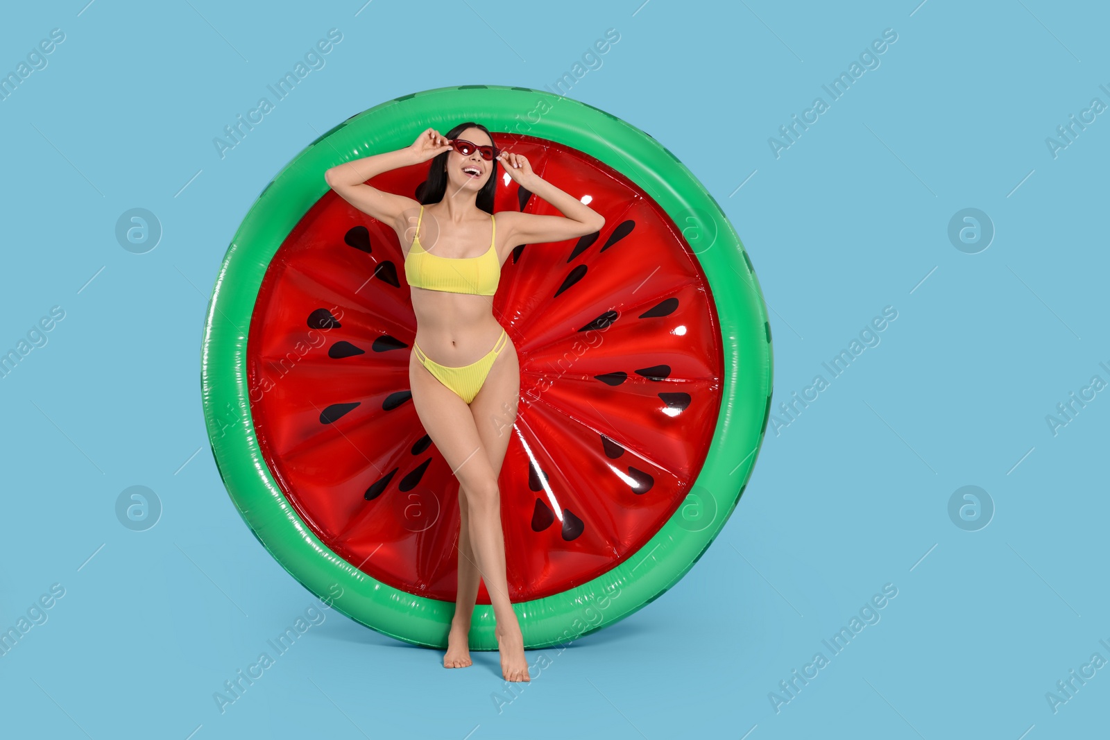 Photo of Young woman in stylish swimsuit near inflatable mattress against light blue background