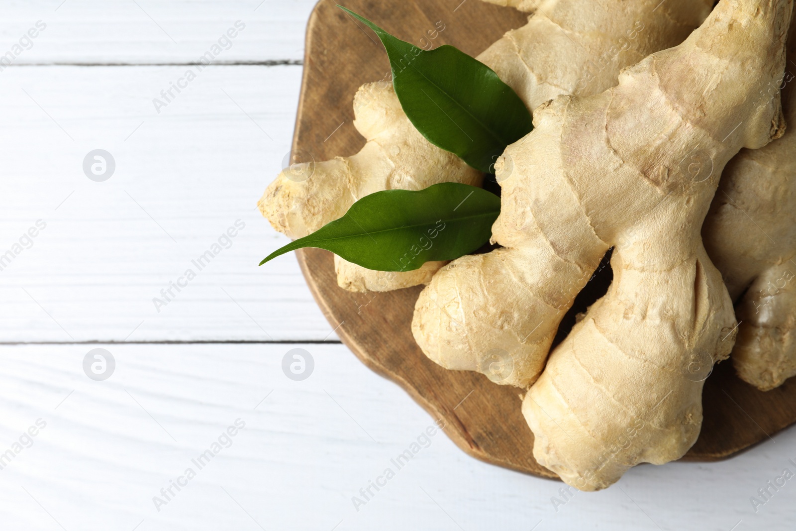 Photo of Fresh ginger with leaves on white wooden table, top view. Space for text