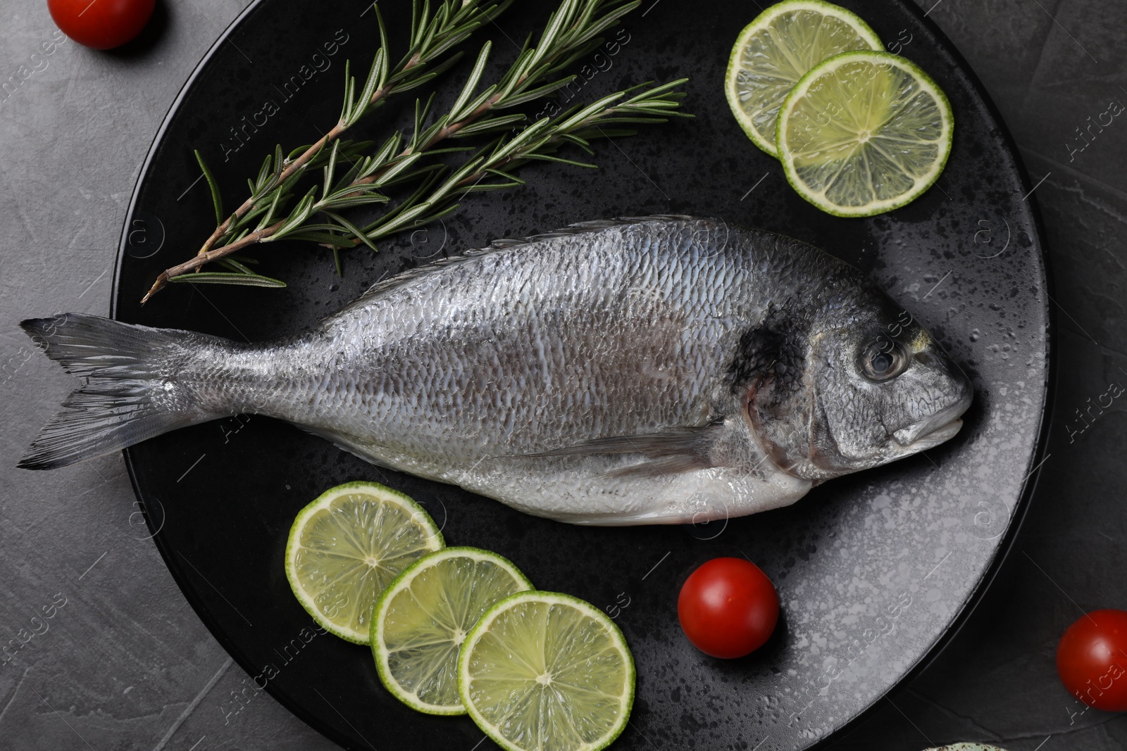 Photo of Fresh dorado fish, lime, tomatoes and rosemary on grey table, top view