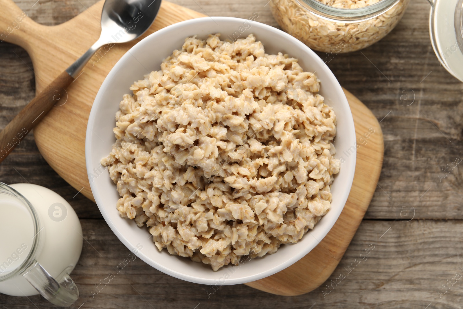 Photo of Tasty boiled oatmeal served on wooden table, flat lay