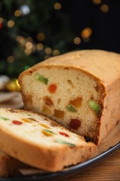Photo of Delicious cake with candied fruits on wooden table against Christmas lights, closeup