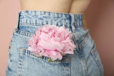 Photo of Woman with pink peony bud in pocket on beige background, closeup