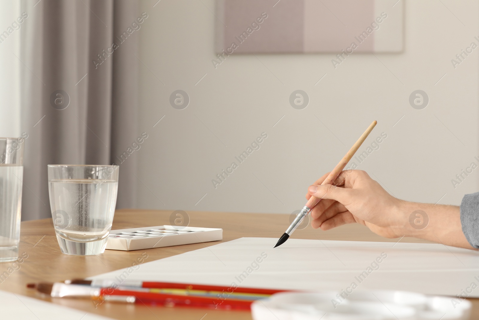 Photo of Woman with brush and paint at wooden table indoors, closeup. Watercolor artwork