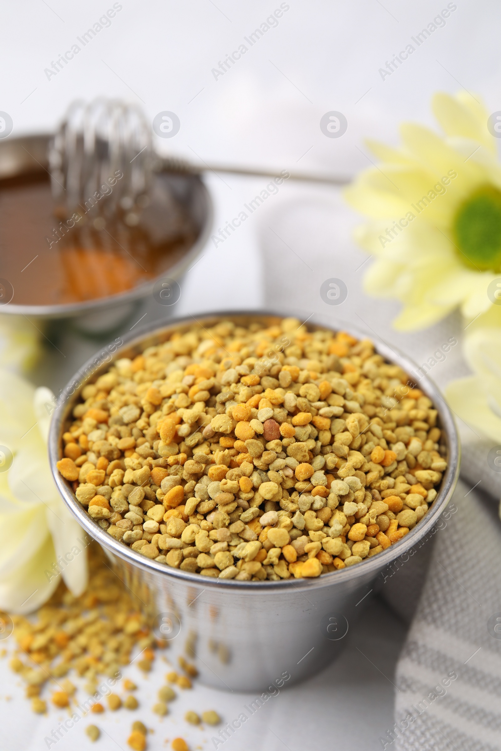 Photo of Fresh bee pollen granules and flowers on white table, closeup