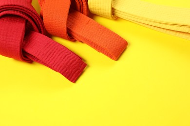 Colorful karate belts on yellow background, flat lay. Space for text