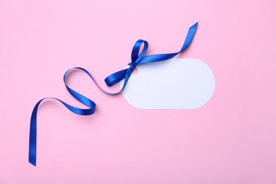 Blank gift tag with satin ribbon on color background, top view