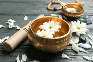 Photo of Golden singing bowl with flowers and mallet on grey wooden table, closeup. Sound healing