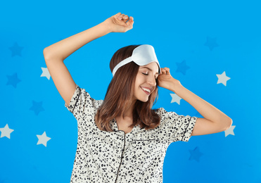 Photo of Beautiful woman wearing pajamas and sleep mask on light blue background. Bedtime