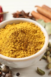 Photo of Curry powder in bowl and other spices on white wooden table, closeup