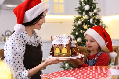 Mother and daughter with gingerbread house indoors