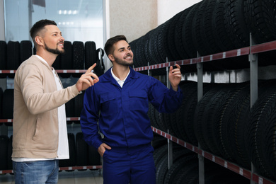 Mechanic helping client to choose car tire in auto store