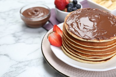 Photo of Tasty pancakes with chocolate paste and berries on white marble table, space for text