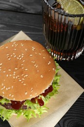 Photo of Burger with delicious patty and soda drink on black wooden table