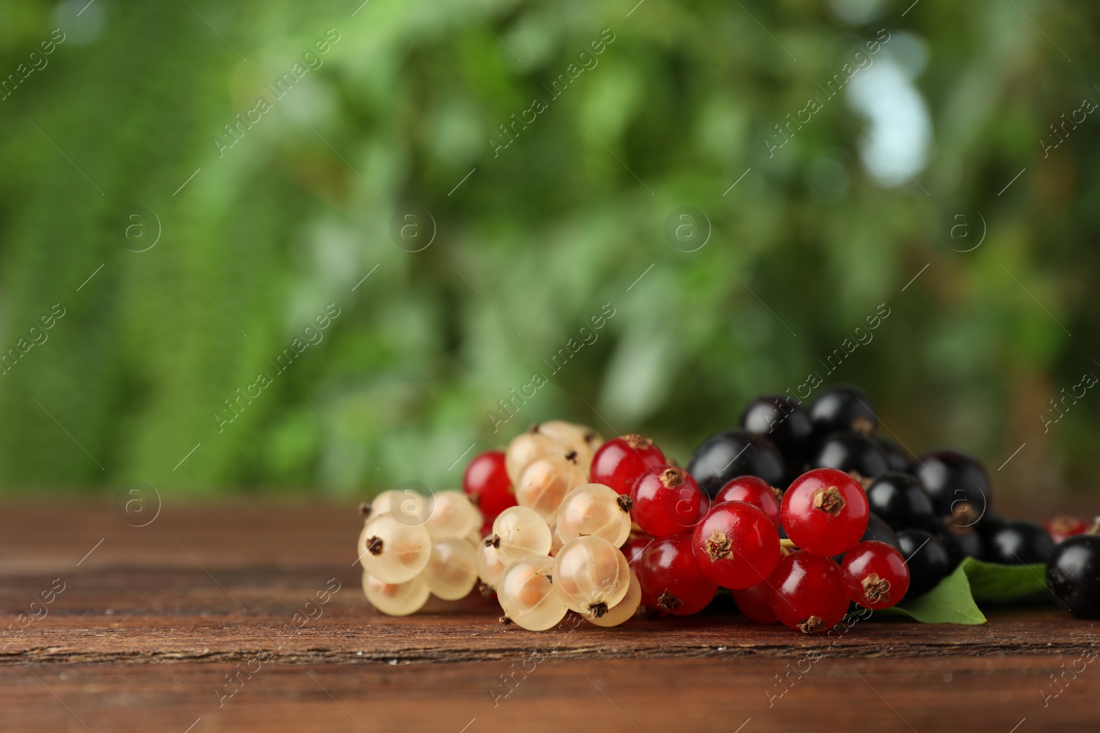 Photo of Different fresh ripe currants on wooden table outdoors, closeup. Space for text