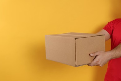 Photo of Courier holding cardboard box on yellow background, closeup. Space for text