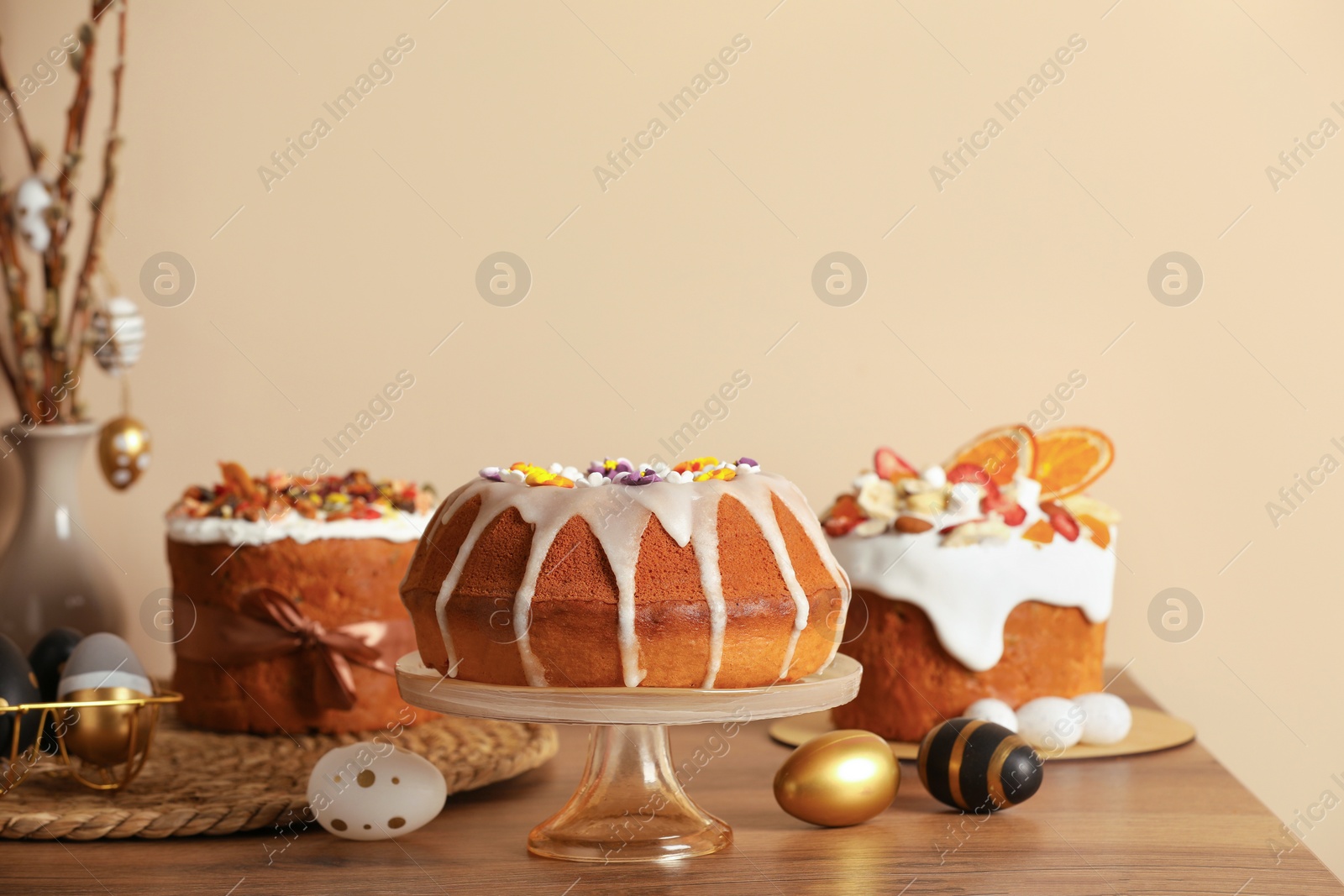 Photo of Delicious Easter cakes decorated with sprinkles near painted eggs on wooden table