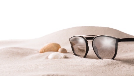 Photo of Stylish sunglasses and shells on sand against white background. Space for text