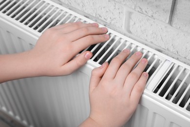 Photo of Girl warming hands on heating radiator indoors, closeup