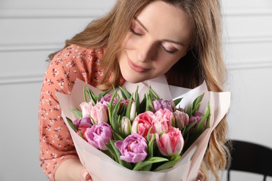 Photo of Happy young woman with bouquet of beautiful tulips indoors