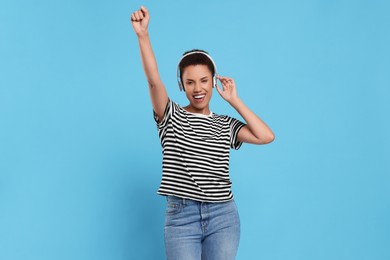Happy young woman in headphones dancing on light blue background