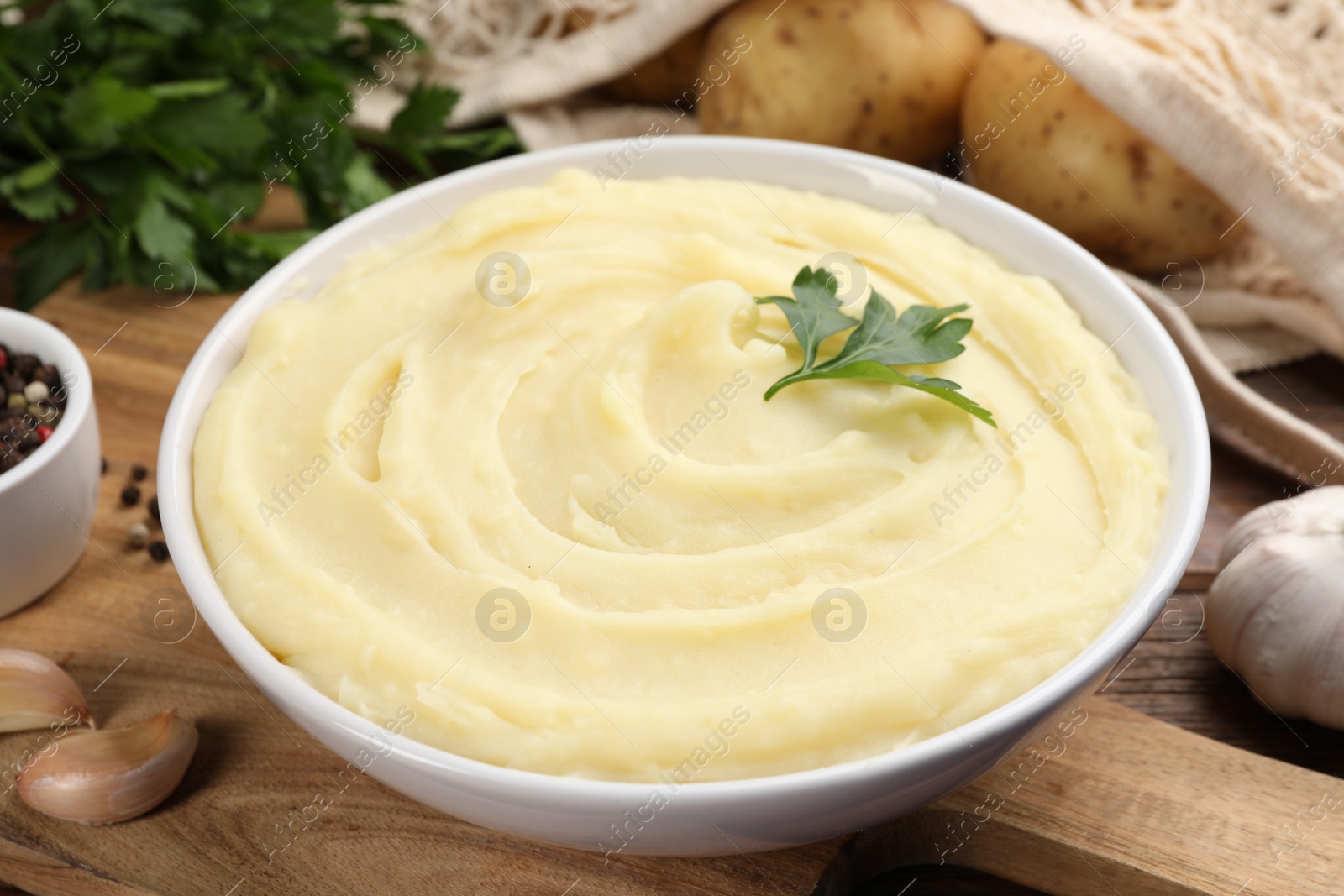 Photo of Bowl of tasty mashed potato, parsley, garlic and pepper on wooden table, closeup