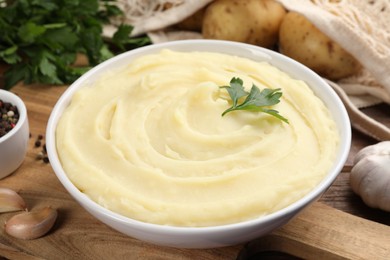 Bowl of tasty mashed potato, parsley, garlic and pepper on wooden table, closeup