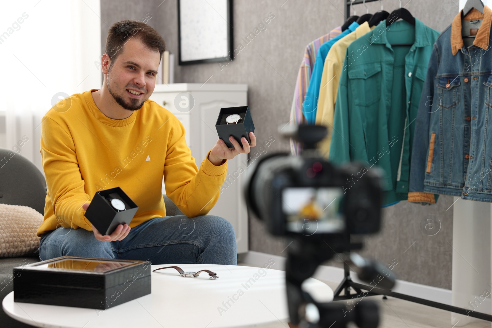Photo of Smiling fashion blogger showing wristwatches while recording video at home