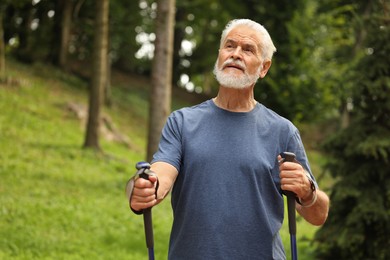 Photo of Senior man with Nordic walking poles outdoors, space for text