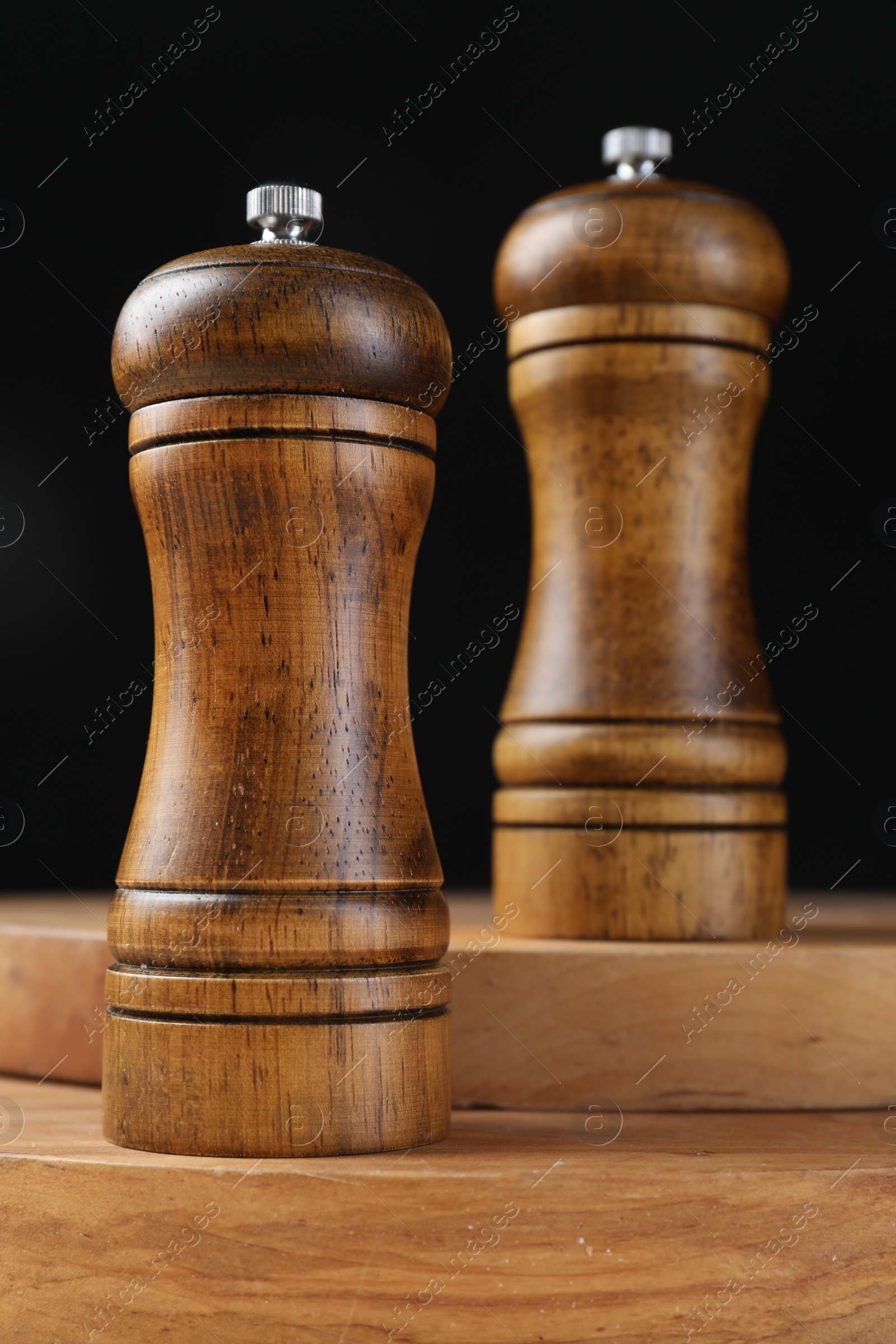 Photo of Salt and pepper shakers on wooden table against black background, closeup