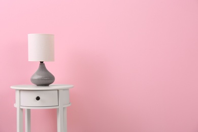 Photo of Stylish lamp on table against color background. Space for text