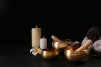 Photo of Composition with golden singing bowls on black table against dark background, space for text