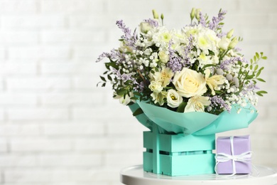 Photo of Beautiful bouquet of flowers and gift box on table against light background. Space for text