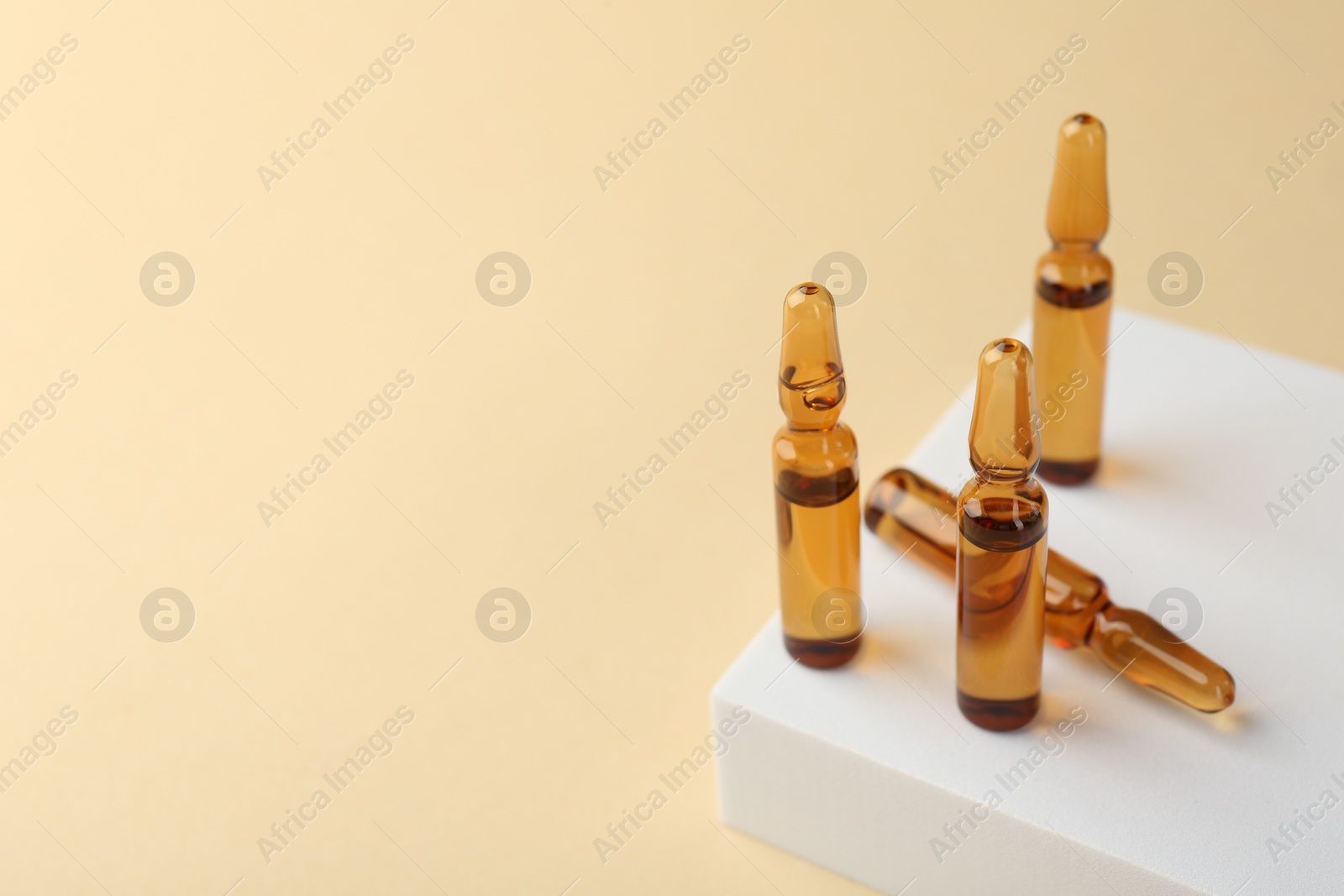 Photo of Glass ampoules with liquid on beige background. Space for text