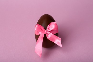 Photo of Tasty chocolate egg with bow on pink background, top view