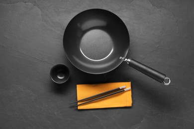 Empty iron wok, sauce bowl and chopsticks on black table, flat lay