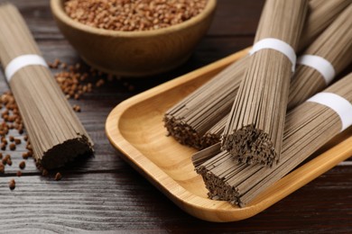Uncooked buckwheat noodles (soba) and grains on wooden table, closeup