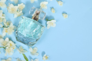 Aromatic perfume in bottle and beautiful jasmine flowers on light blue background, flat lay. Space for text