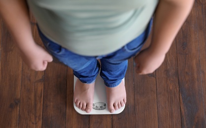 Overweight boy standing on floor scales indoors, above view