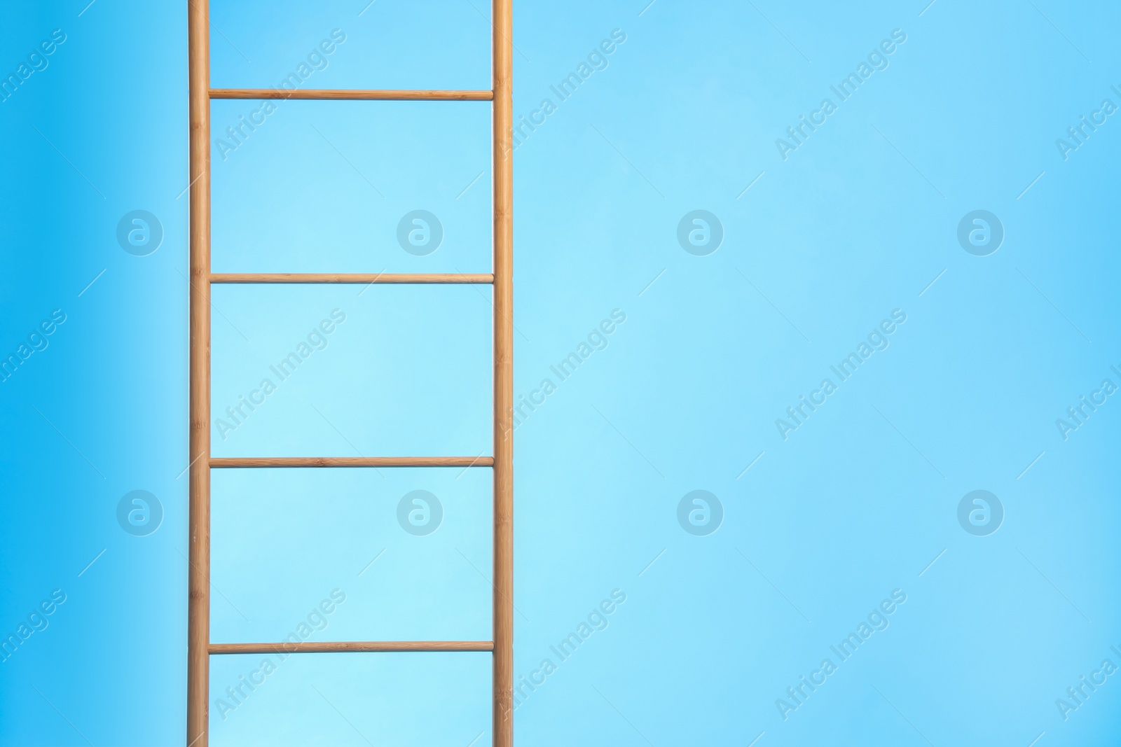 Photo of Modern wooden ladder on light blue background. Space for text