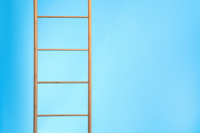 Modern wooden ladder on light blue background. Space for text