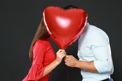 Photo of Couple kissing while hiding behind heart shaped balloon on dark background
