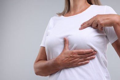 Woman doing breast self-examination on light grey background, closeup. Space for text