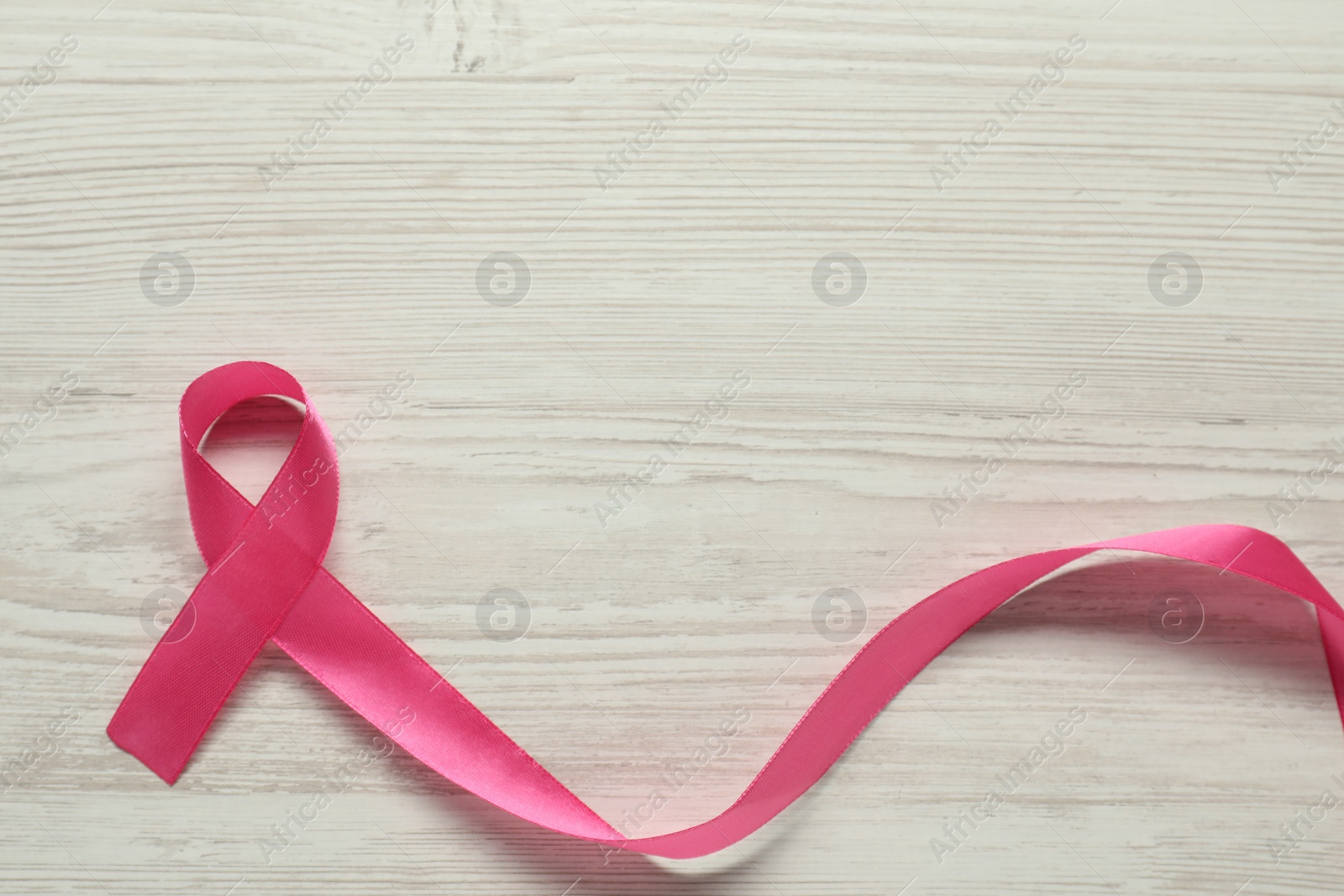 Photo of Breast cancer awareness. Pink ribbon on white wooden table, top view. Space for text