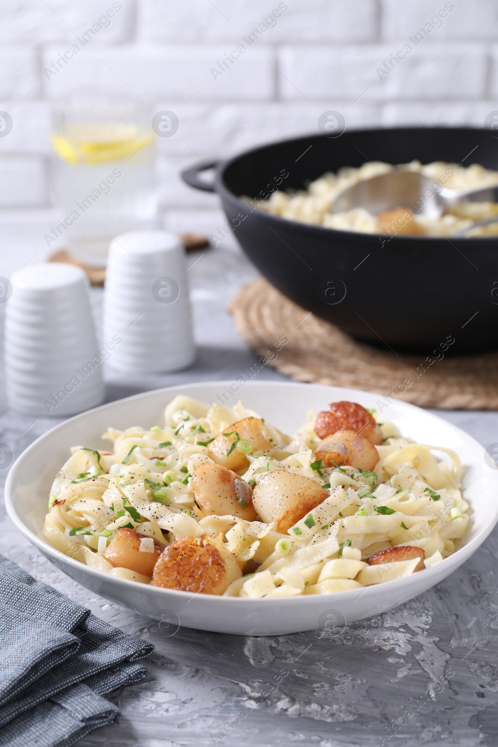 Photo of Delicious scallop pasta with spices in bowl on gray textured table