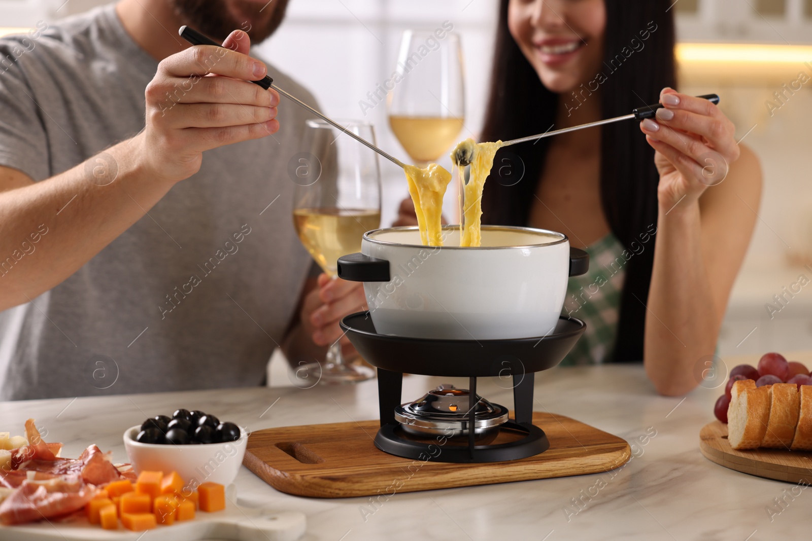 Photo of Couple enjoying cheese fondue during romantic date indoors, closeup