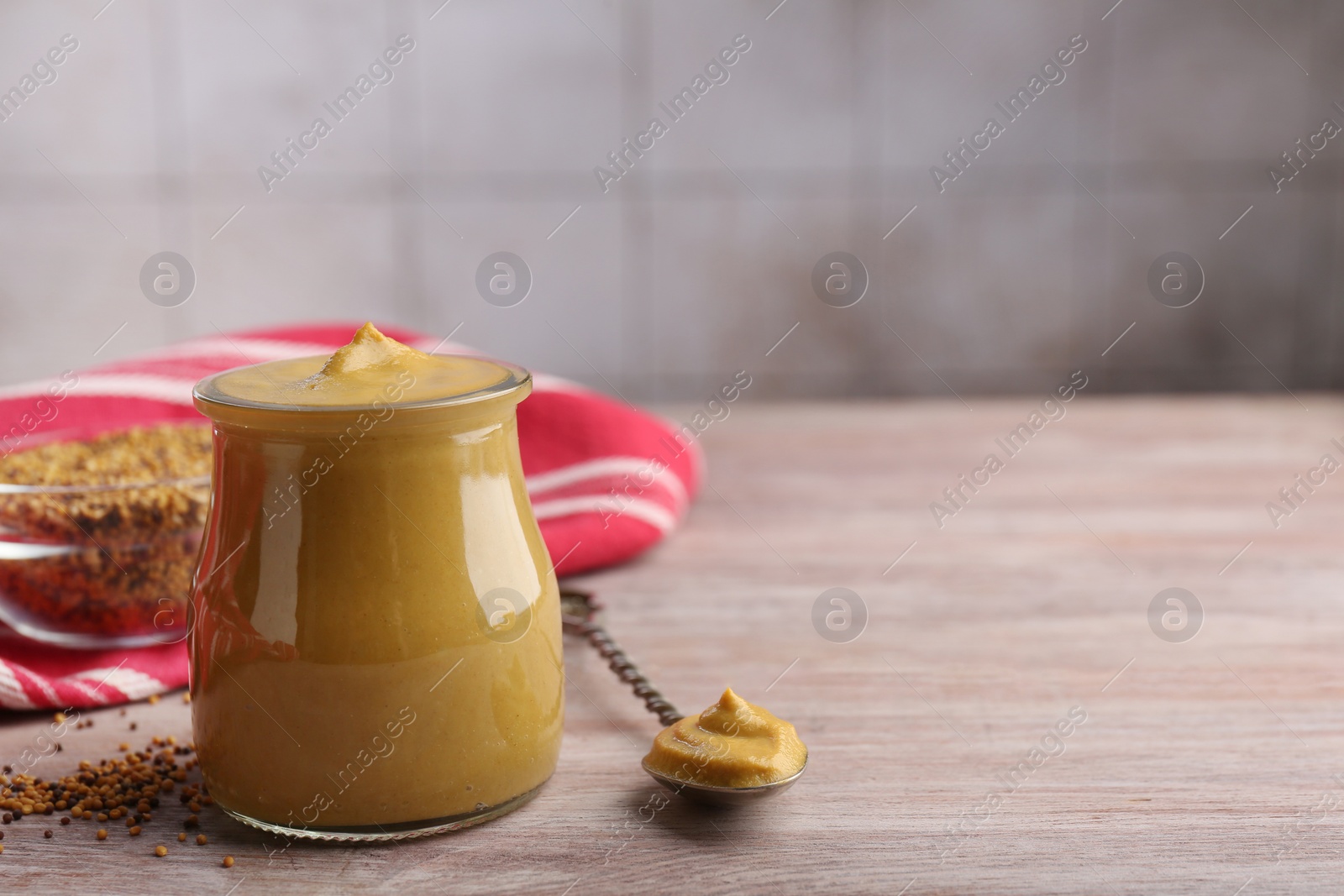 Photo of Jar and spoon with tasty mustard sauce on wooden table, space for text