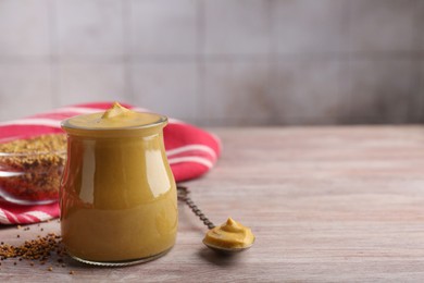 Photo of Jar and spoon with tasty mustard sauce on wooden table, space for text