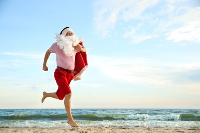 Photo of Santa Claus having fun on beach, space for text. Christmas vacation
