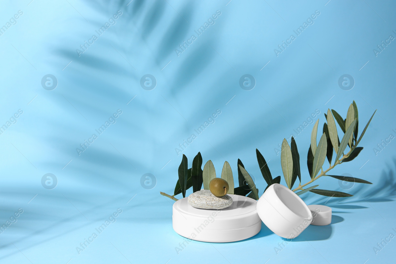 Photo of Jars of olive cream on light blue background, space for text. Cosmetic products