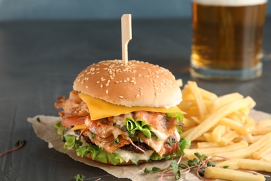 Tasty burger with bacon and French fries on table